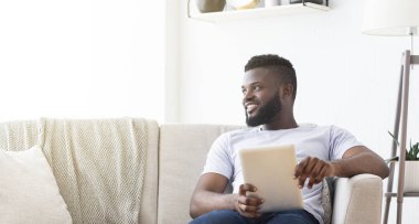 Cheerful african man resting at home with digital tablet