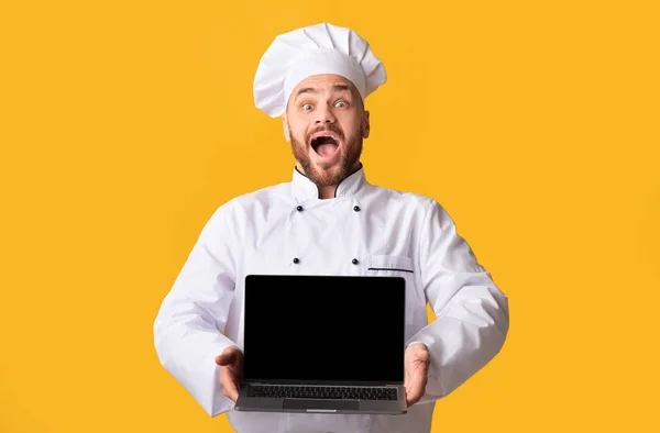 Animado masculino chef mostrando laptop em branco tela, fundo amarelo — Fotografia de Stock