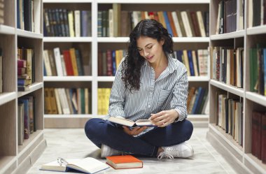 Smiling latina girl reading books at library