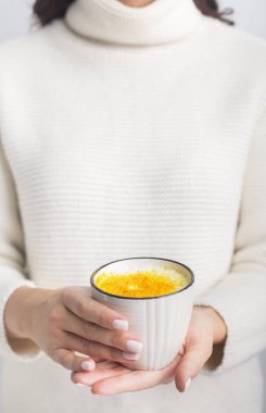 Female in sweater holding turmeric milk with powder