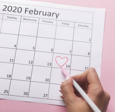 Woman painting heart on Date February 14 on calendar
