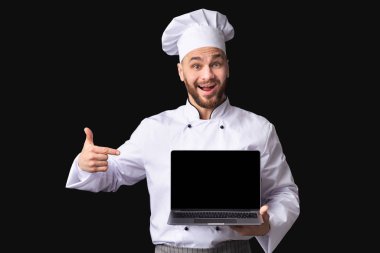 Male Chef Showing Laptop Pointing Finger At Screen, Black Background
