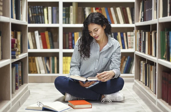 Sonriente chica latina leyendo libros en la biblioteca — Foto de Stock