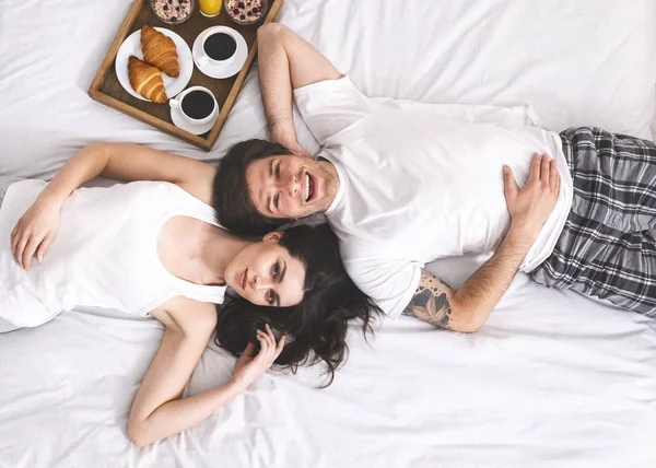 Soții tineri fericiți întinși în pat cu tavă de mic dejun — Fotografie, imagine de stoc