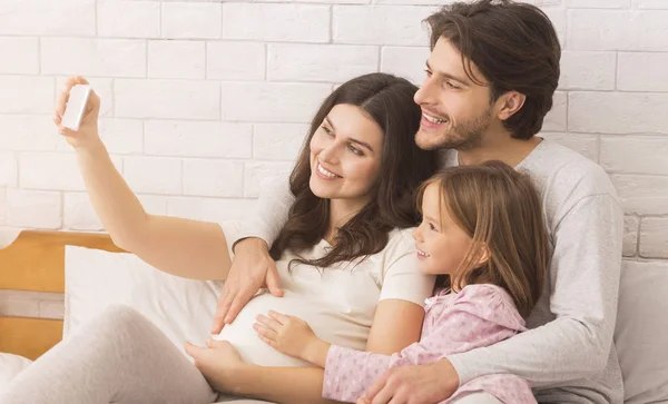 Mulher grávida tomando auto-retrato com marido e filha bonito no quarto — Fotografia de Stock