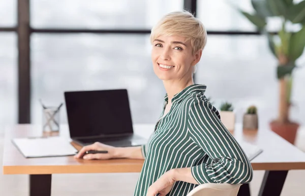 Mujer de negocios sentada en el ordenador portátil sonriendo a la cámara posando en el lugar de trabajo — Foto de Stock