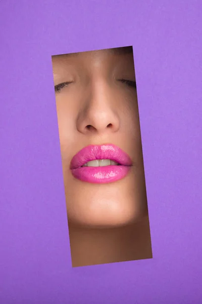 Girl with plump pink lips through hole in purple paper — ストック写真