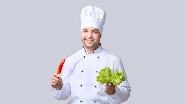 Chef tenant le poivre et les feuilles de salade debout, fond gris, Panorama — Photo