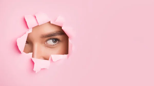 Beautiful woman with natural makeup looking through torn paper