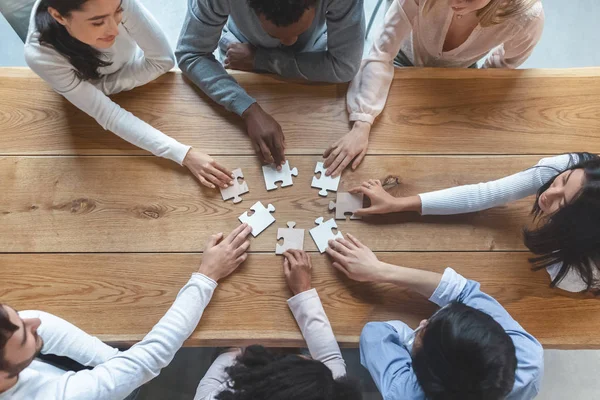 Équipe multiraciale assise autour de la table, rassemblant des pièces de puzzle — Photo