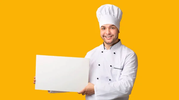 Chef sosteniendo afiche blanco en blanco de pie sobre fondo amarillento, Panorama — Foto de Stock