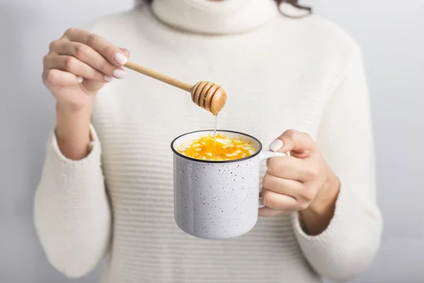 Woman drinking golden turmeric milk with honey over gray — ストック写真