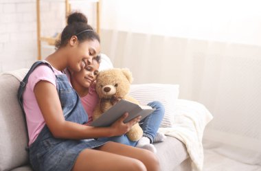 Two african sisters reading fairy tale book at home