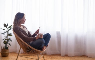Calm woman networking on smartphone, sitting with cocoa