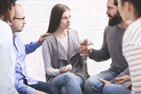 Therapy group members comforting upset woman at community meeting in rehab