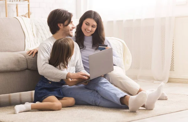 Happy family sitting on floor indoors with laptop and credit card