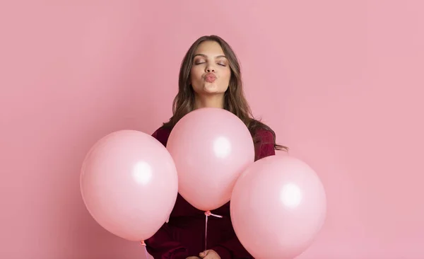 Chica juguetona sosteniendo globos rosados y labios de pucheros, enviando beso de aire — Foto de Stock