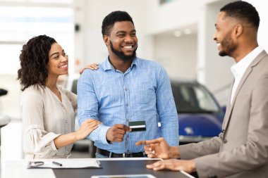 Couple Buying Car Giving Seller Credit Card In Dealership Office