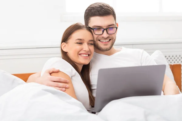 Pareja con ordenador portátil viendo película y abrazando acostado en la cama —  Fotos de Stock