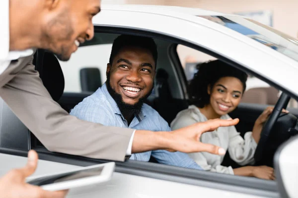 Casal feliz comprando carro conversando com vendedor sentado em automóvel — Fotografia de Stock