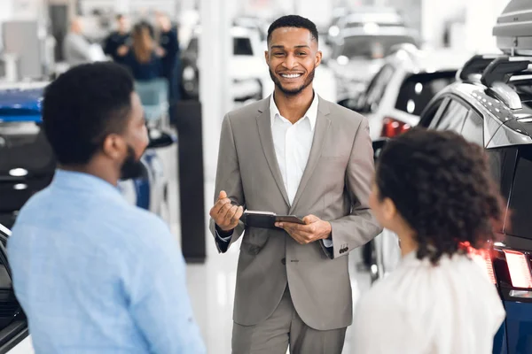 Concessionário de carros conversando com clientes vendendo automóvel na loja de concessionárias — Fotografia de Stock