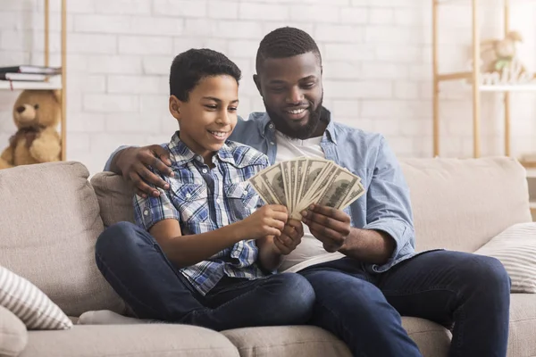 Joven hombre negro contando dinero en efectivo del dólar con su hijo, explicándole la precisión financiera — Foto de Stock