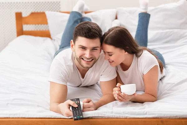 Alegre namorado e namorada assistindo TV juntos deitado na cama — Fotografia de Stock