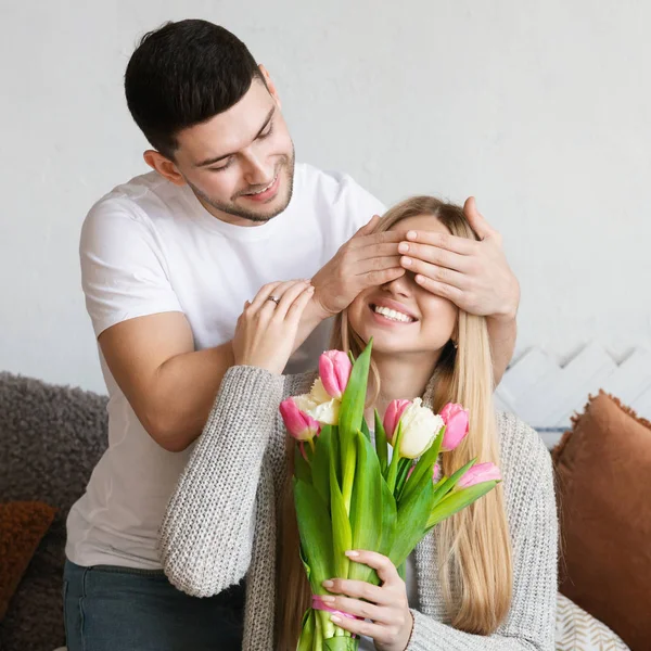Hombre regalando a su esposa tulipanes flores y cubría sus ojos — Foto de Stock