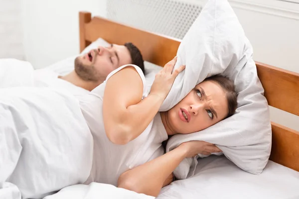Муж храпит надоедливая разгневанная жена лежит в постели в помещении — стоковое фото