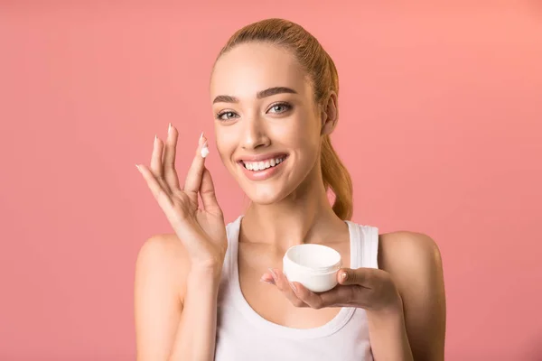 Girl Applying Facial Cream Holding Jar Standing On Pink Background — Stockfoto