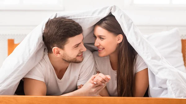 Casal segurando as mãos deitado coberto com cobertor no quarto, Panorama — Fotografia de Stock