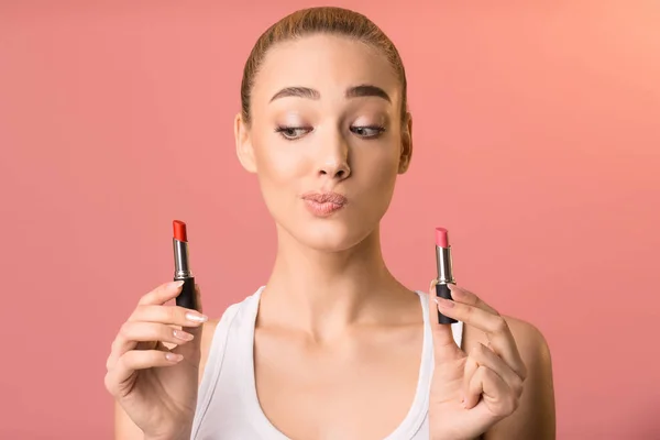 Schöne Frau wählt Lippenstift für Make-up stehend auf rosa Hintergrund — Stockfoto
