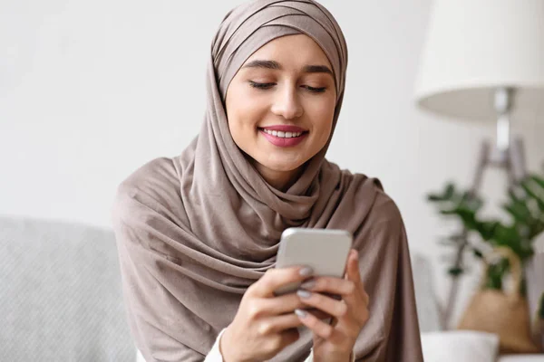 (Inggris) Modern Muslim Girl In Hijab Typing Message On Smartphone At Home — Stok Foto