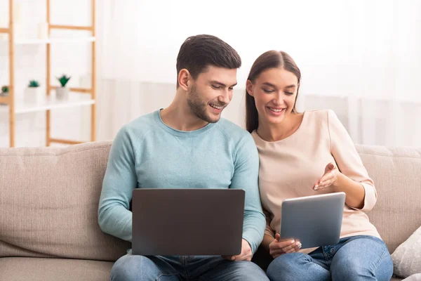 Laptopot és tabletet használó házaspár otthon ül a kanapén — Stock Fotó