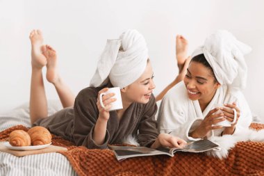 Smiling women in bathrobes and towels laying on bed