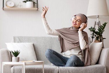Joyful muslim girl in headphones enjoying favorite music at home