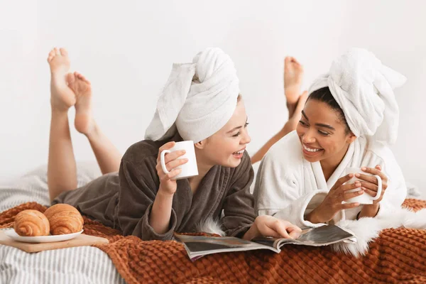 Mulheres sorridentes em roupões de banho e toalhas deitadas na cama — Fotografia de Stock