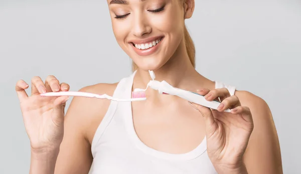 Menina aplicando pasta de dentes na escova de dentes sobre fundo de estúdio cinza . — Fotografia de Stock