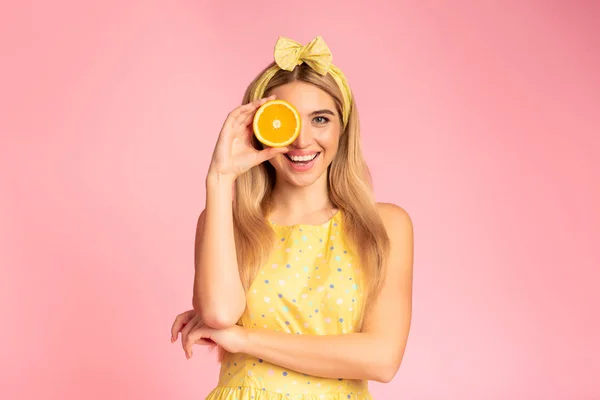 Blonde girl holding orange slice next to eye — ストック写真