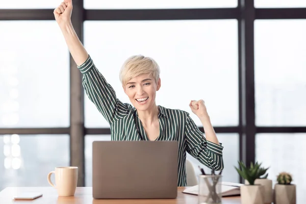 Empresária de meia-idade feliz balançando punhos sentados no escritório moderno — Fotografia de Stock