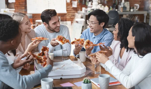 Vriendelijk internationaal team genieten van pizza samen in kantoor — Stockfoto