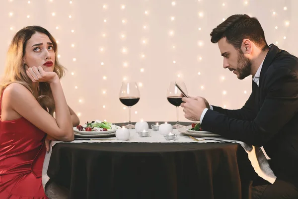 Unhappy woman sitting alone while her boyfriend stuck into his phone — Stok fotoğraf