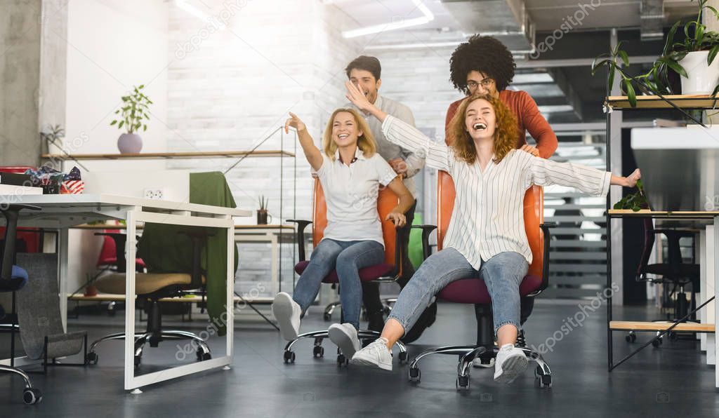 Carefree young colleagues having chair race competition in office