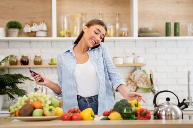 Woman multitasking at kitchen, talking on phone and cooking