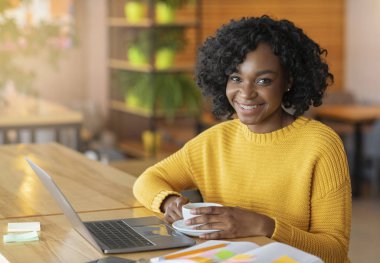 Portrait of black young cheerful lady using laptop at cafeteria