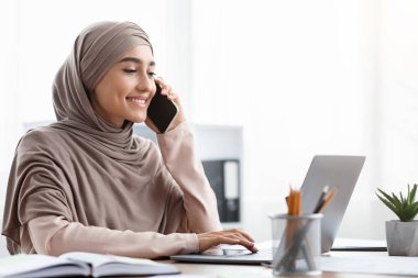 Islamic businesslady talking on cellphone and working with laptop in office