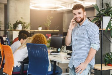 Young cheerful guy talking by phone during working time
