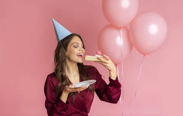 Joyeux anniversaire fille manger gâteau, debout sur fond rose avec des ballons — Photo