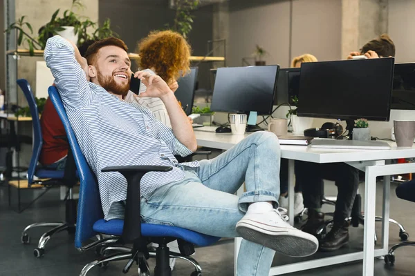 Young relaxed man talking on phone in modern coworking