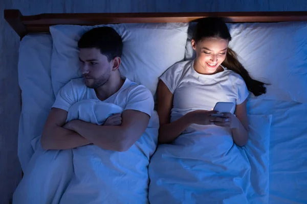 Cheating Girlfriend Texting Lying Near Boyfriend In Bed, Top View — Stok fotoğraf